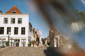 Couple embracing on cobblestone street in charming Dutch town with white historic buildings on sunny day.