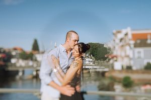 Couple sharing a romantic kiss near a waterfront with boats and buildings in the background on a sunny day. Leiden