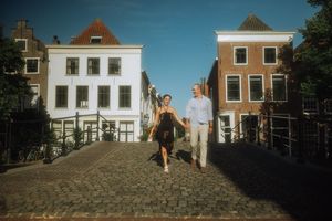 Couple walking hand in hand over a cobblestone bridge in a charming Dutch town Leiden with historic white buildings.