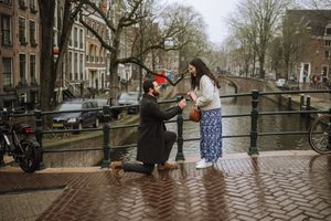 Man proposing to woman on one knee on a canal bridge in Amsterdam, Netherlands.