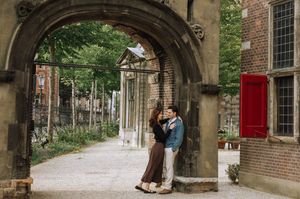 Couple embracing under a stone arch in Amsterdam, surrounded by lush greenery and historic brick buildings.