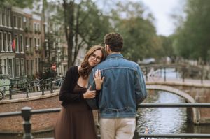 Couple hugging on a bridge over an Amsterdam canal, with charming Dutch architecture in the background.