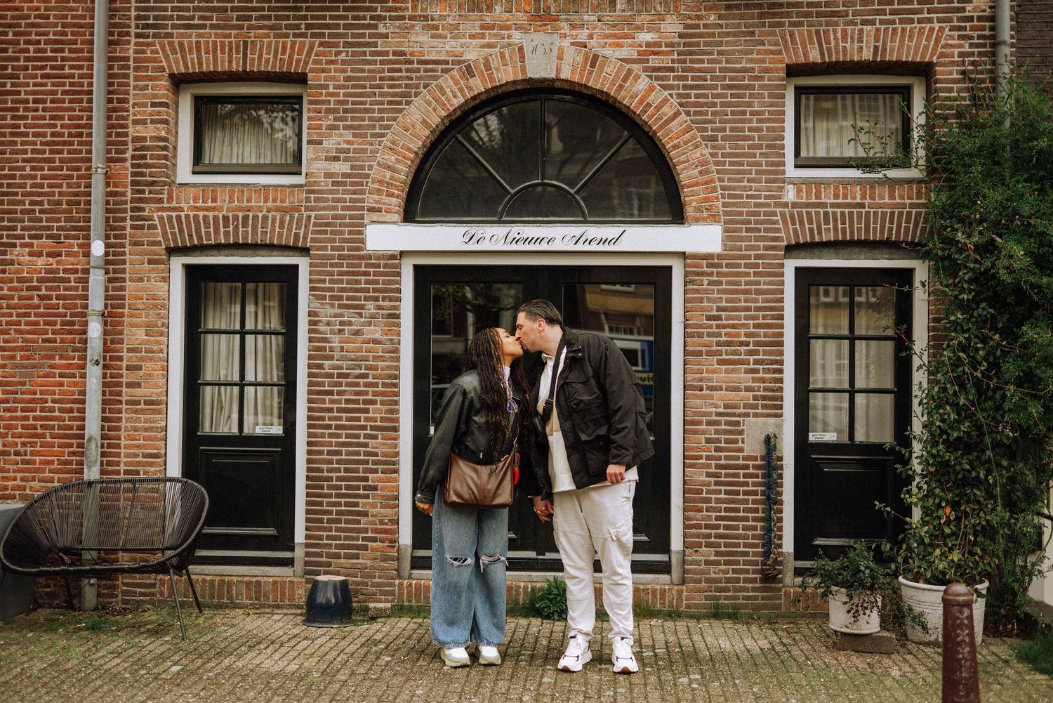 Couple sharing a romantic kiss in front of a charming brick building in the Netherlands.