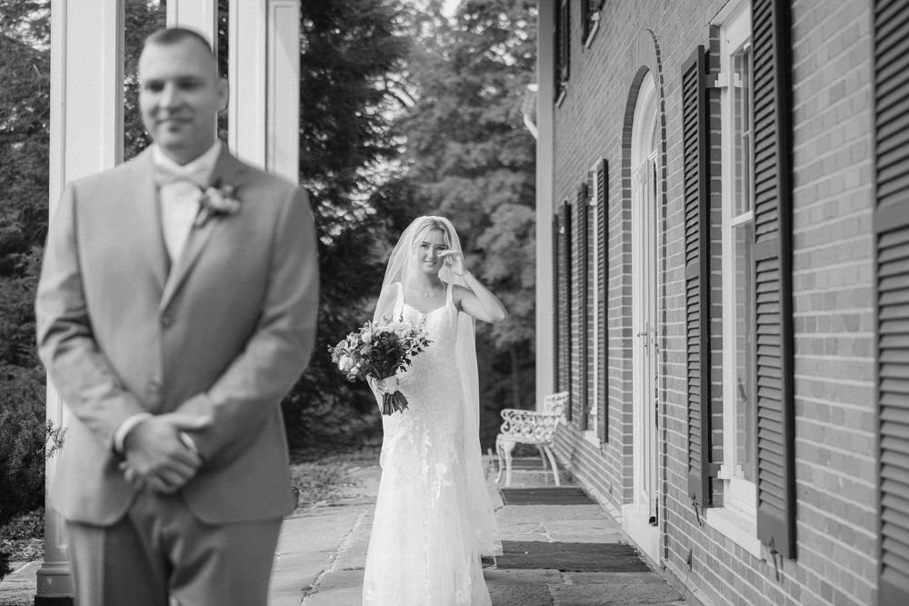 Black and white photo of a bride in a wedding dress approaching a groom in a suit during a first look ceremony.