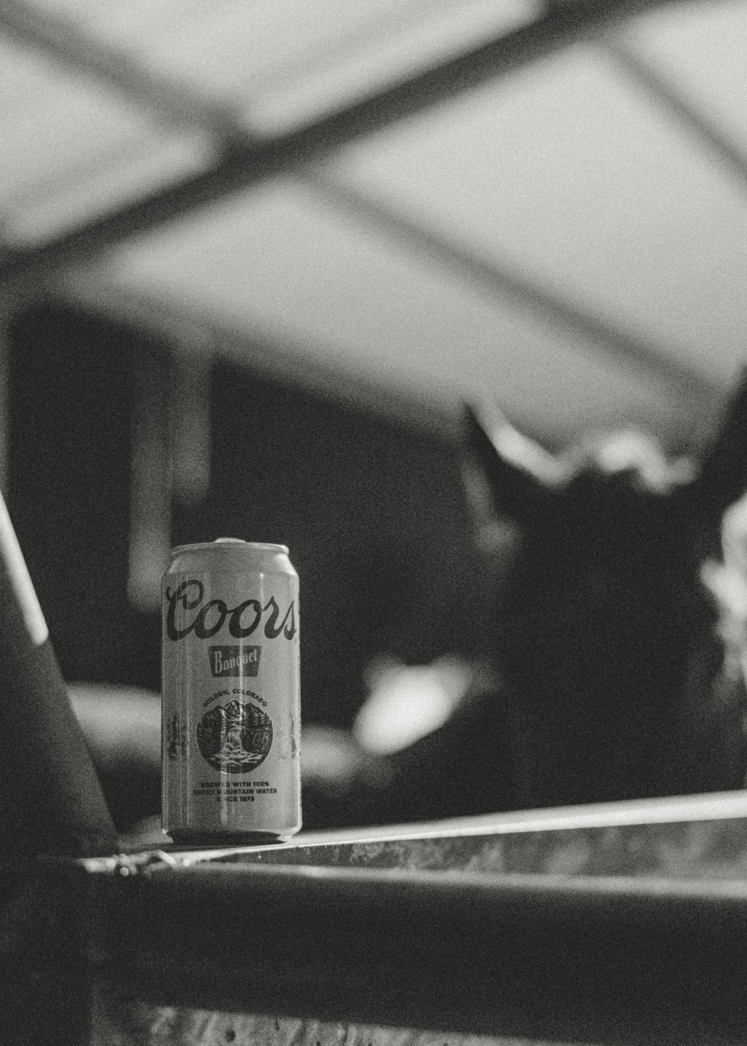 Black and white photo of a Coors beer can resting on a metal rail with a blurred horse's head in the background.