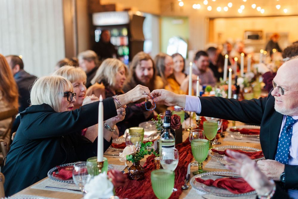 Guests at a festive holiday dinner table clink glasses in a toast beside candles, greenery, and red table decor.