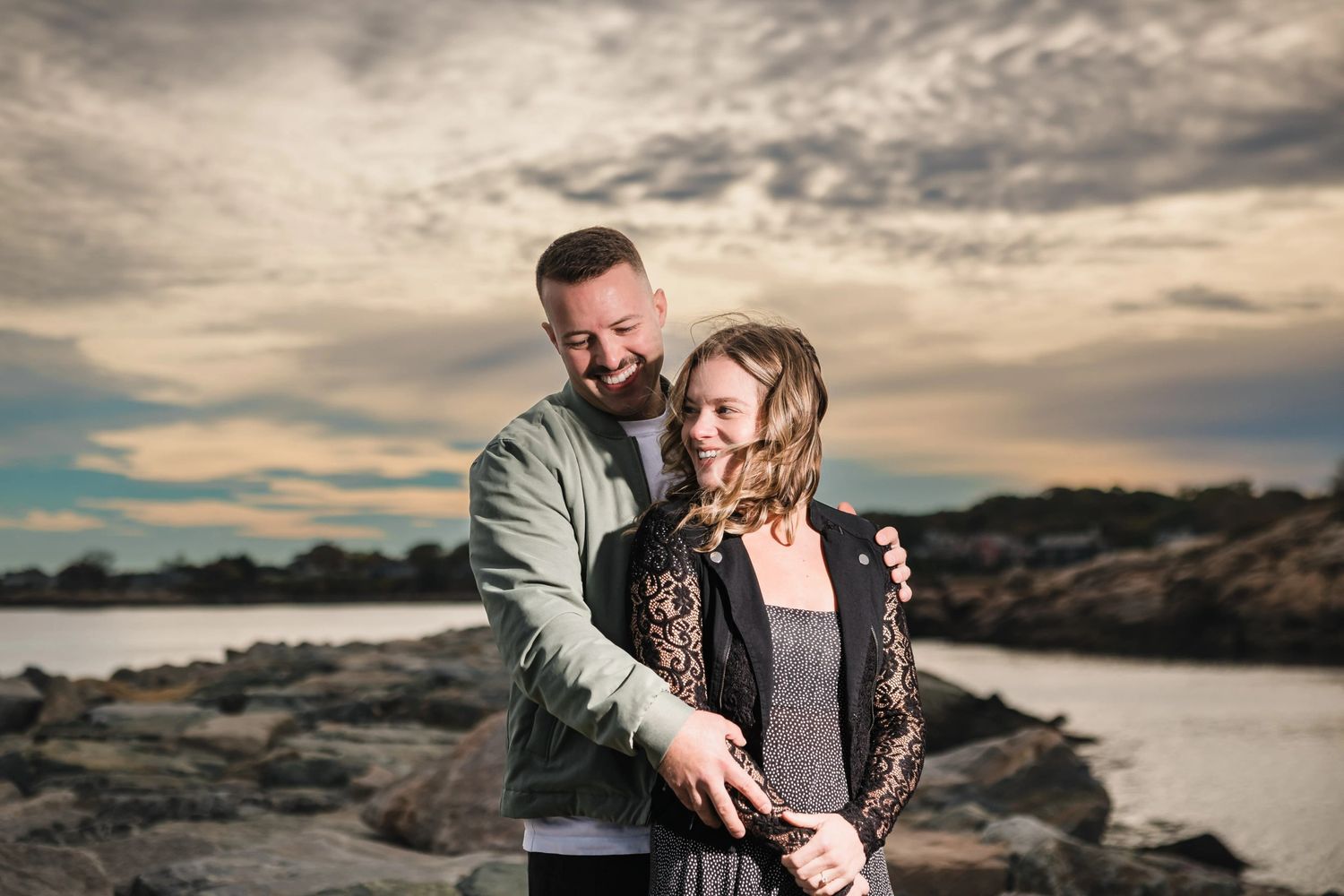 Couple embracing by water, gazing at each at dawn. Engagement at Rockport Harbor, Rockport, MA