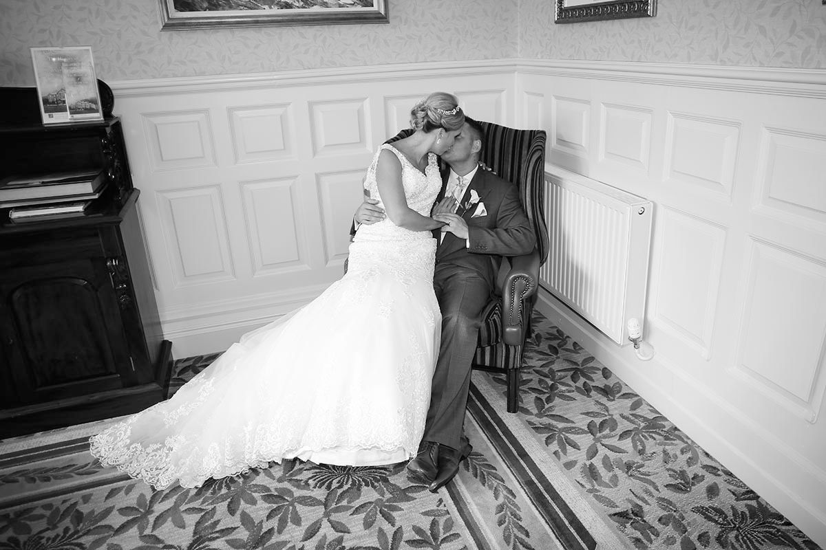 Black and white portrait of the bride and groom sharing a kiss while seated in a panelled room at Inn on the Lake