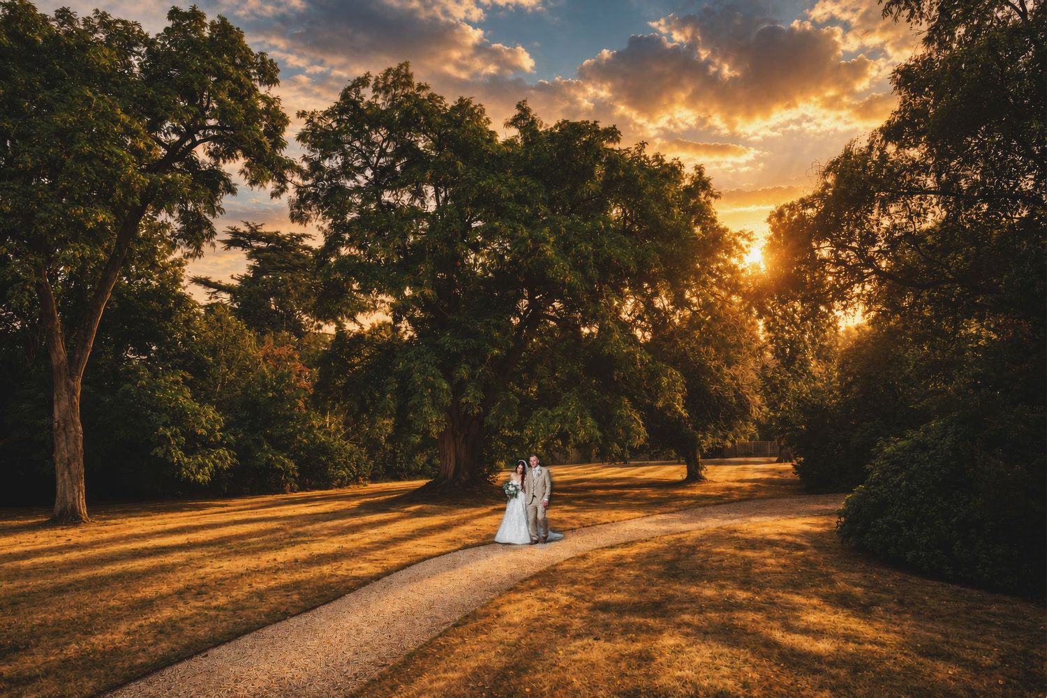 Bride and groom walk at sunset in a lush park, golden light filtering through tall trees on their wedding day.