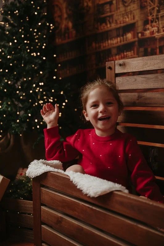 A smiling child in red beside a Christmas tree during a previous photography session.