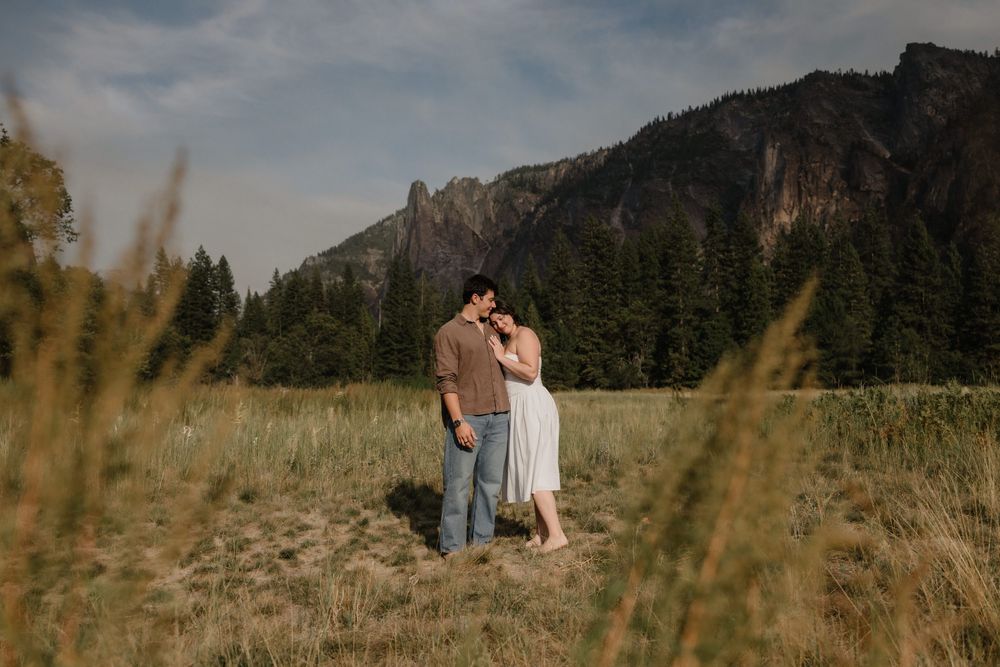 Couple embracing in a golden meadow with pine trees and rocky mountains in Yosemite.