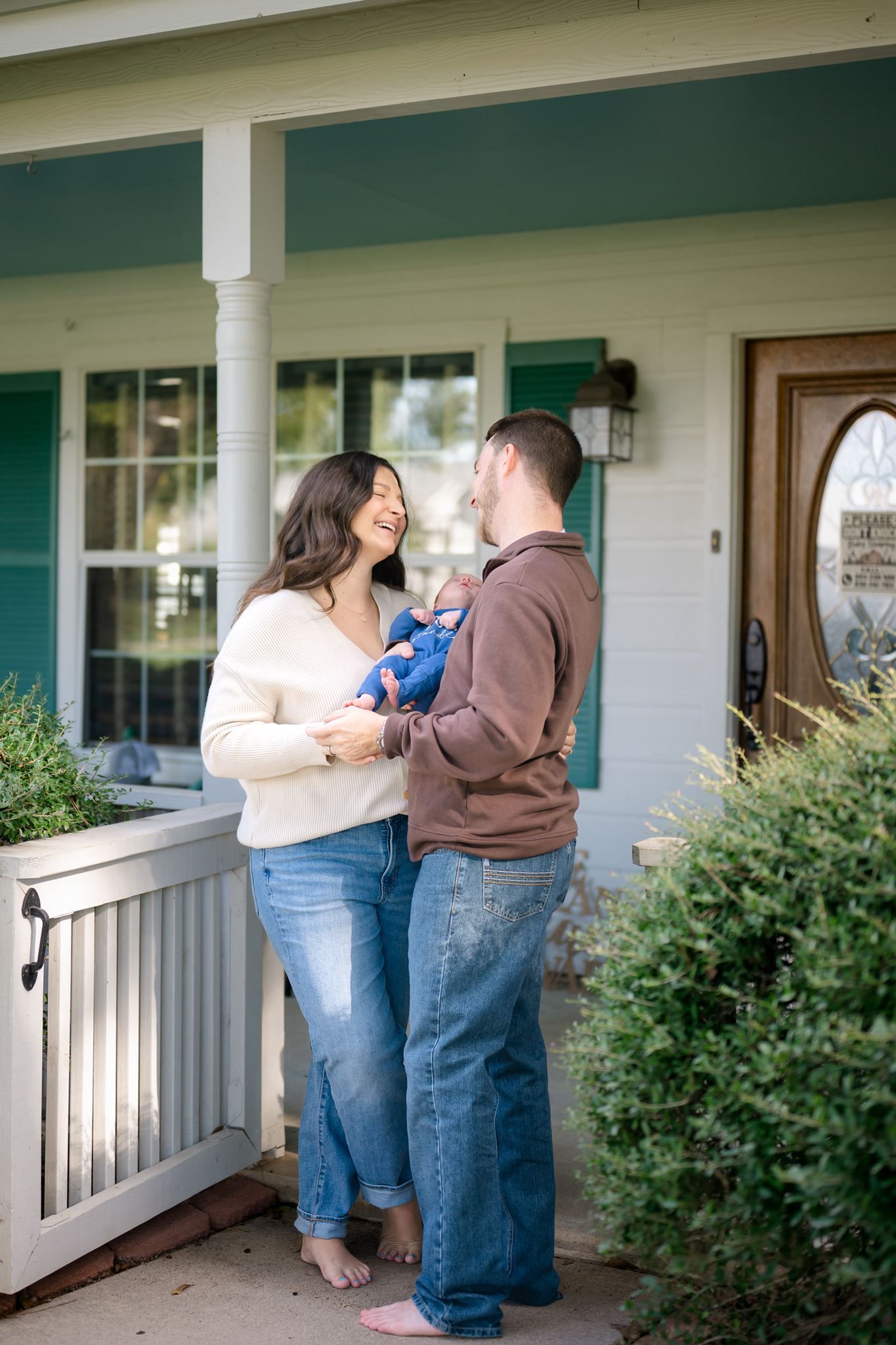 New mother and father holding their newborn on their front porch.