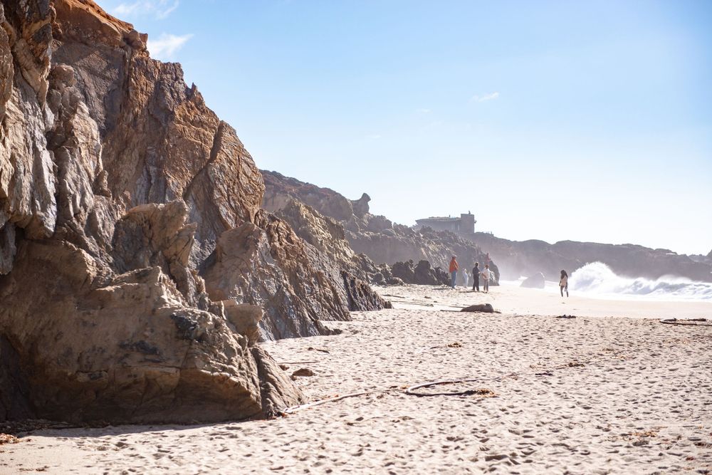 Panoramic sequence of rocky coastal cliffs and sandy beach stretching along a rugged shoreline.