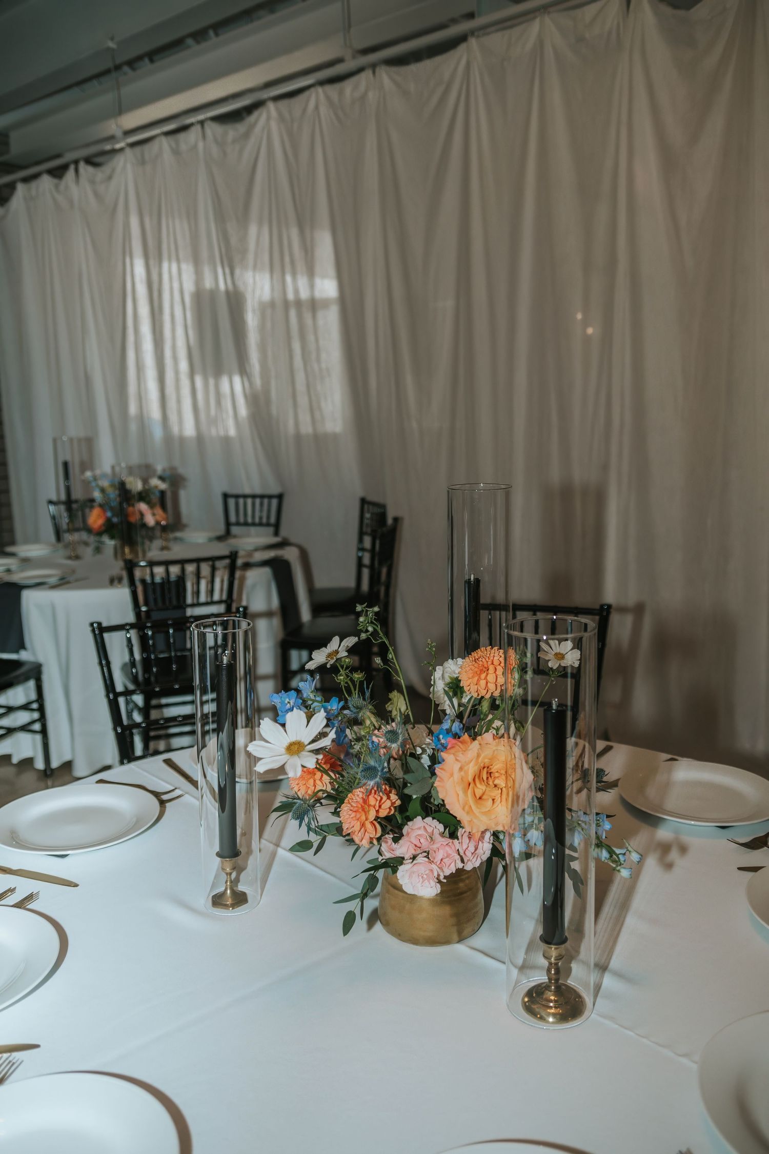 Elegant wedding reception table with gold vase floral centerpiece featuring peach and pink blooms, black candles, and white linens.