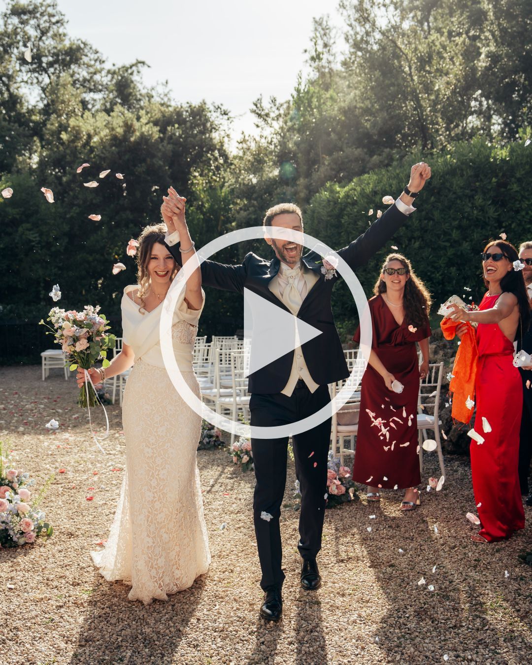 A joyful bride and groom walk down the aisle as guests toss flower petals at an outdoor wedding ceremony.