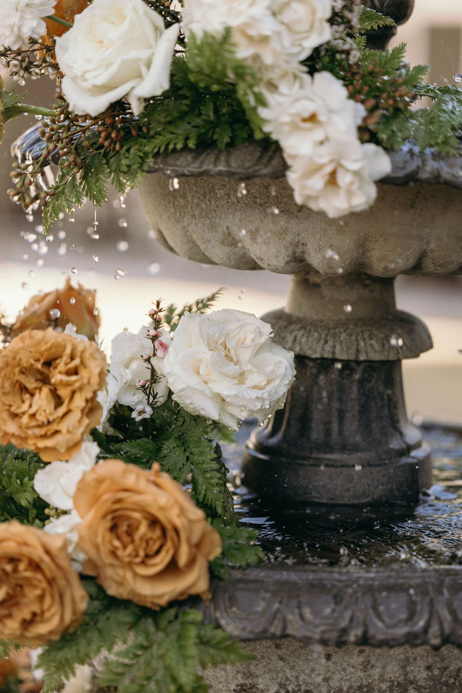 Stone fountain adorned with white and golden roses, ferns, and greenery for an elegant floral display for a winter wedding.