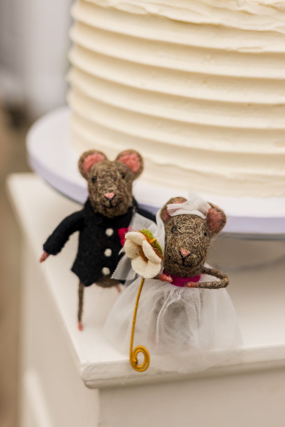 Cute needle felted mouse bride and groom cake toppers beside a white wedding cake.