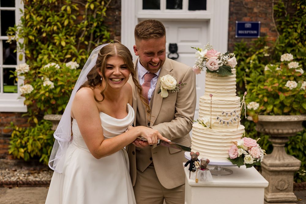 Smiling bride and groom cutting elegant floral wedding cake outdoors.