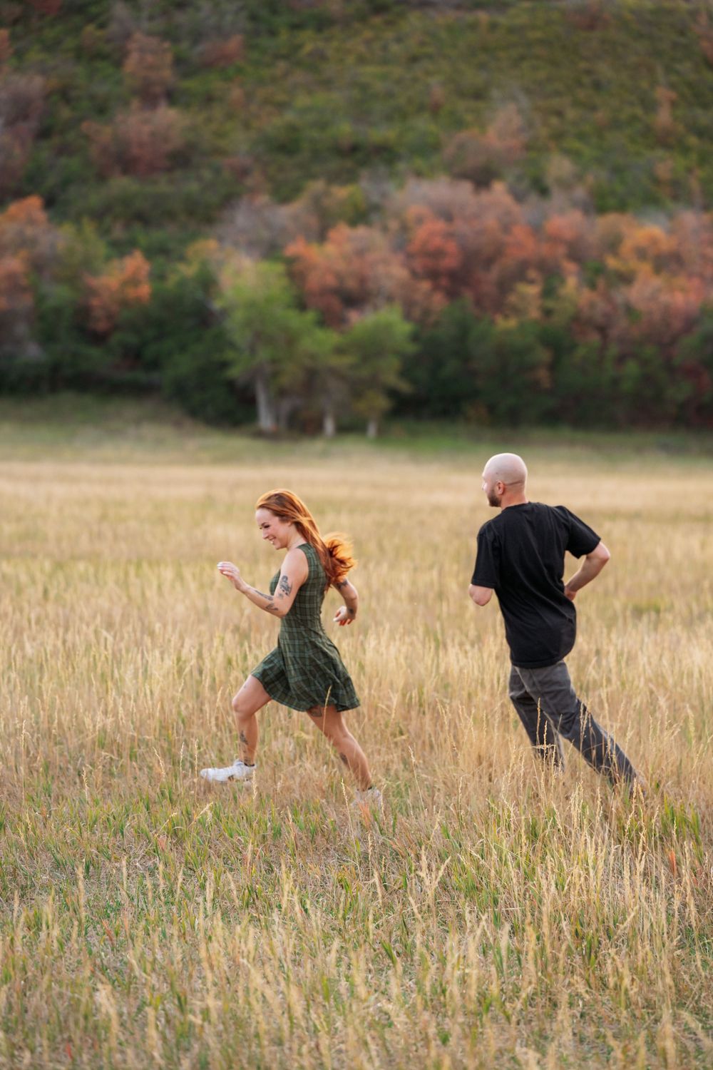 A man and woman jogging together through a golden field with colorful autumn trees in the background.