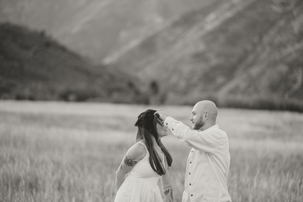 Black and white photo of a couple sharing a tender moment in a mountain meadow, the groom gently touching the bride's face.