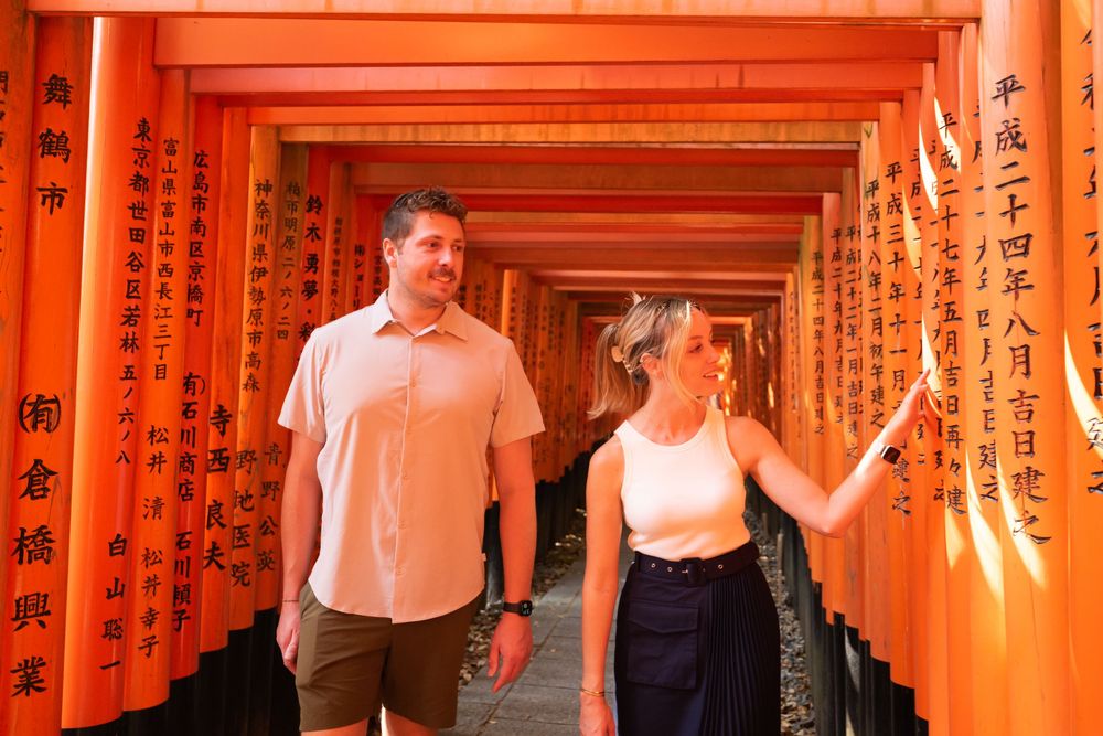 Couple walking through the vermilion torii gates at Fushimi Inari Shrine in Kyoto, Japan, with the woman reaching out to touch a gate.