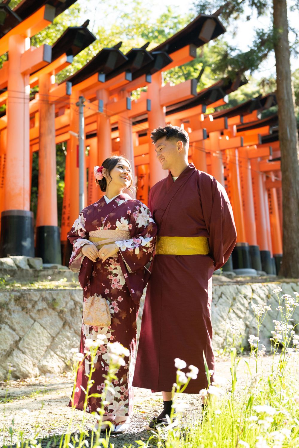 Couple in traditional Japanese kimono embrace and smile beside the vermilion torii gates at Fushimi Inari Shrine in Kyoto.