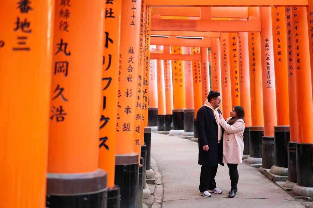 Couple in dark and pink coats walking together through the vermilion torii gates at Fushimi Inari Shrine in Kyoto, Japan.