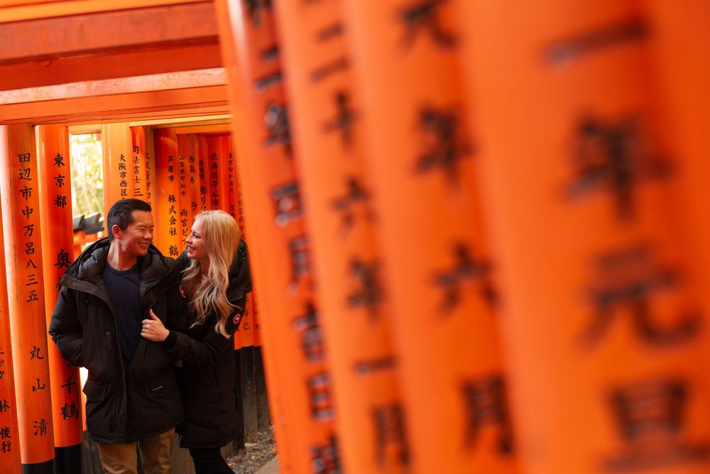 Smiling couple walking arm in arm through the vermilion torii gates of Fushimi Inari Shrine in Kyoto, Japan.