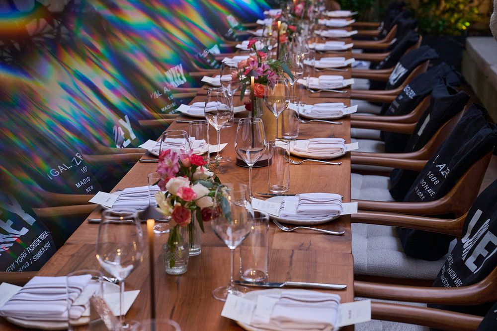 Long wooden banquet table set with white napkins, wine glasses, candles and colorful floral centerpieces in a stylish restaurant dining room