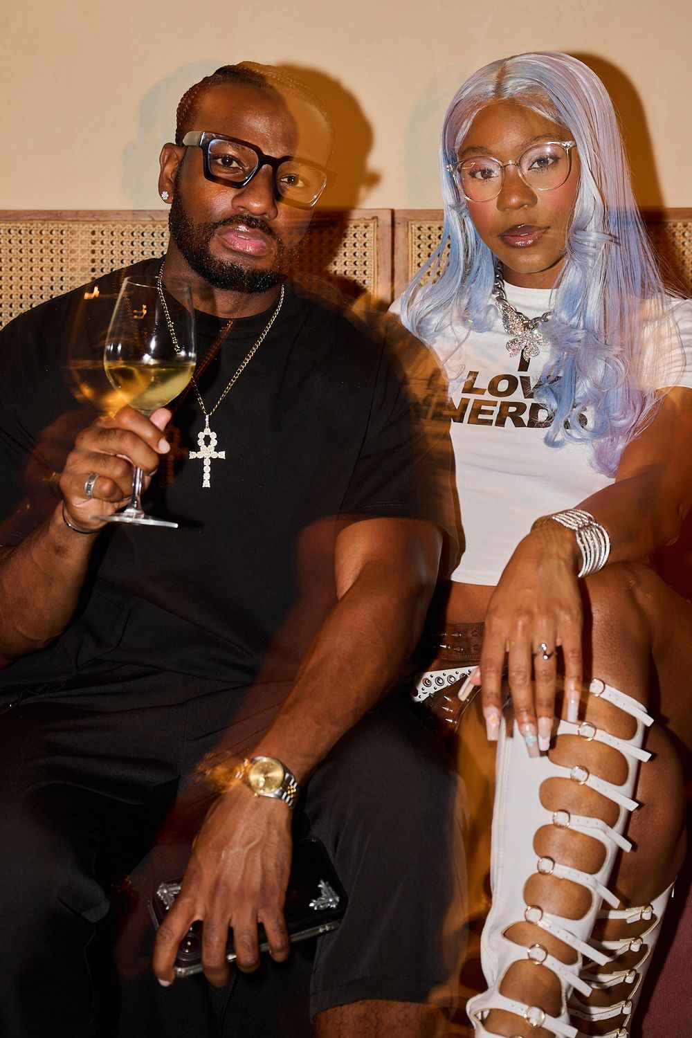 Man in glasses holding a wine glass sits beside a woman with long blue hair in a Love Nerd tee and lace-up white boots.
