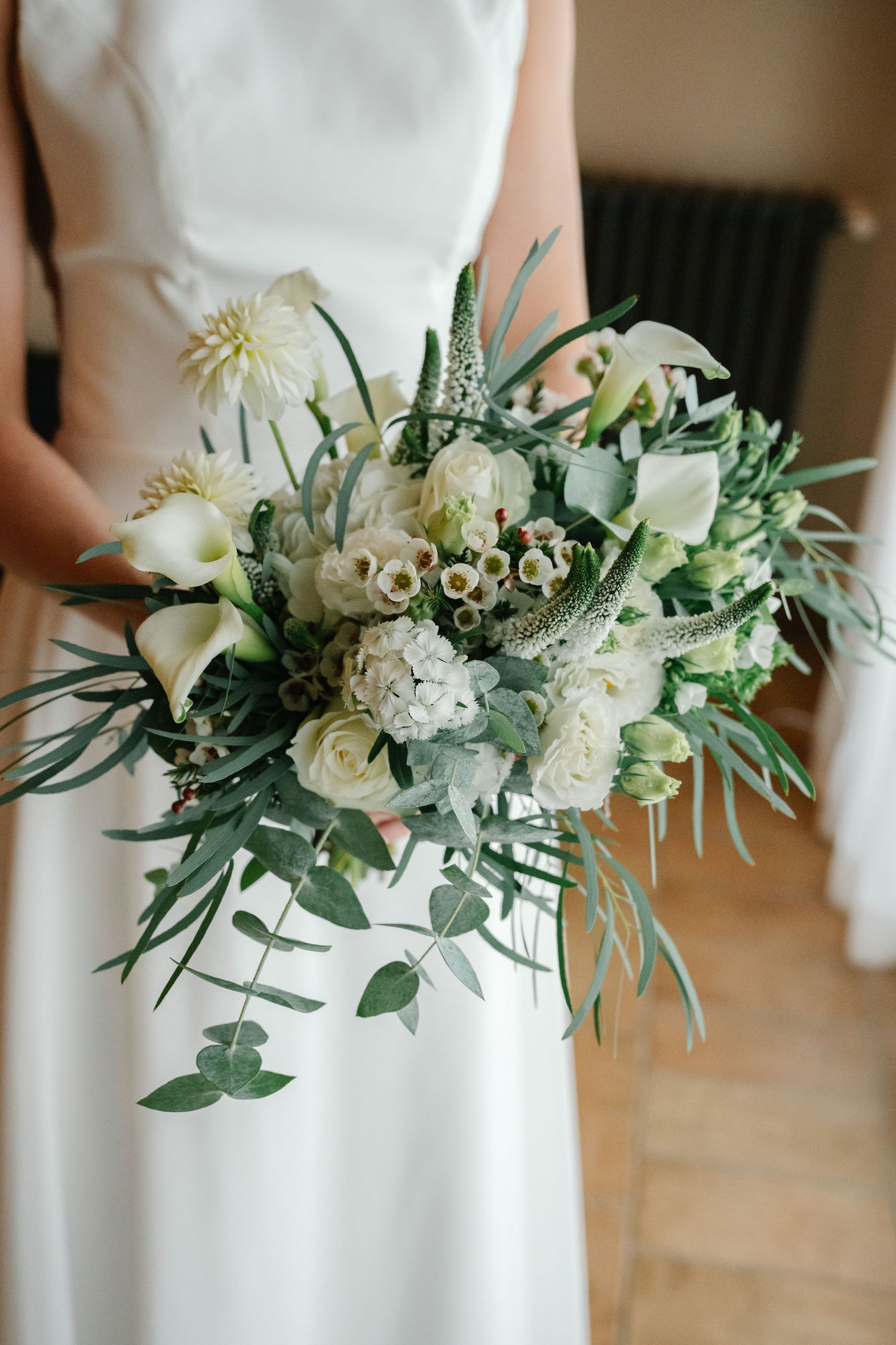 Bride in white gown holding lush wedding bouquet with white roses, calla lilies, and eucalyptus greenery.