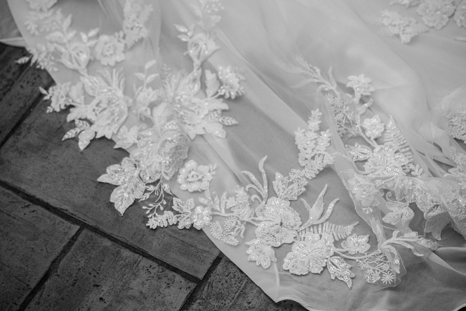 Close-up of intricate floral lace embroidery on a white wedding dress veil, photographed in black and white.