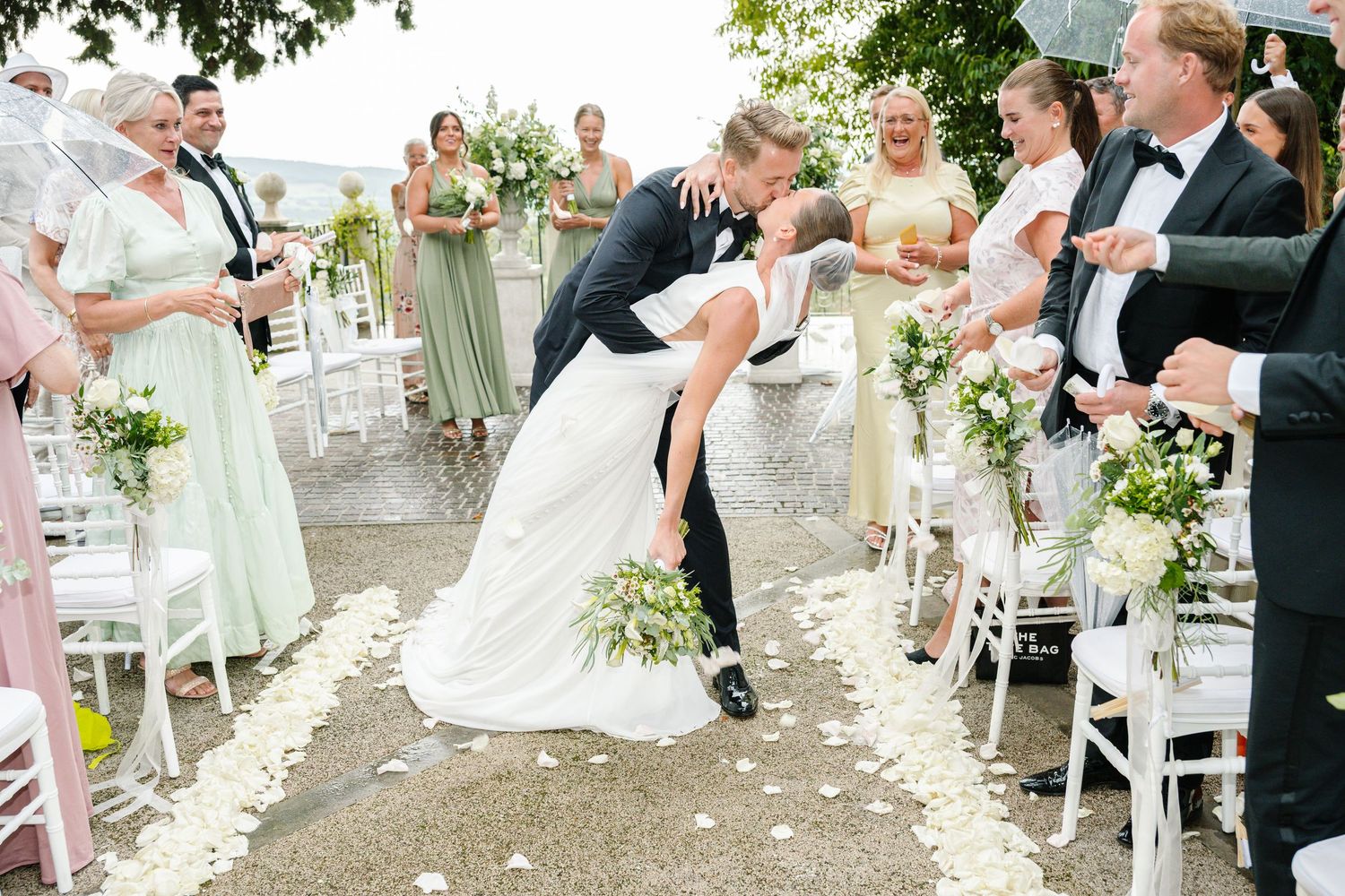 Bride and groom share a romantic dip kiss while walking down the aisle at an outdoor wedding ceremony.