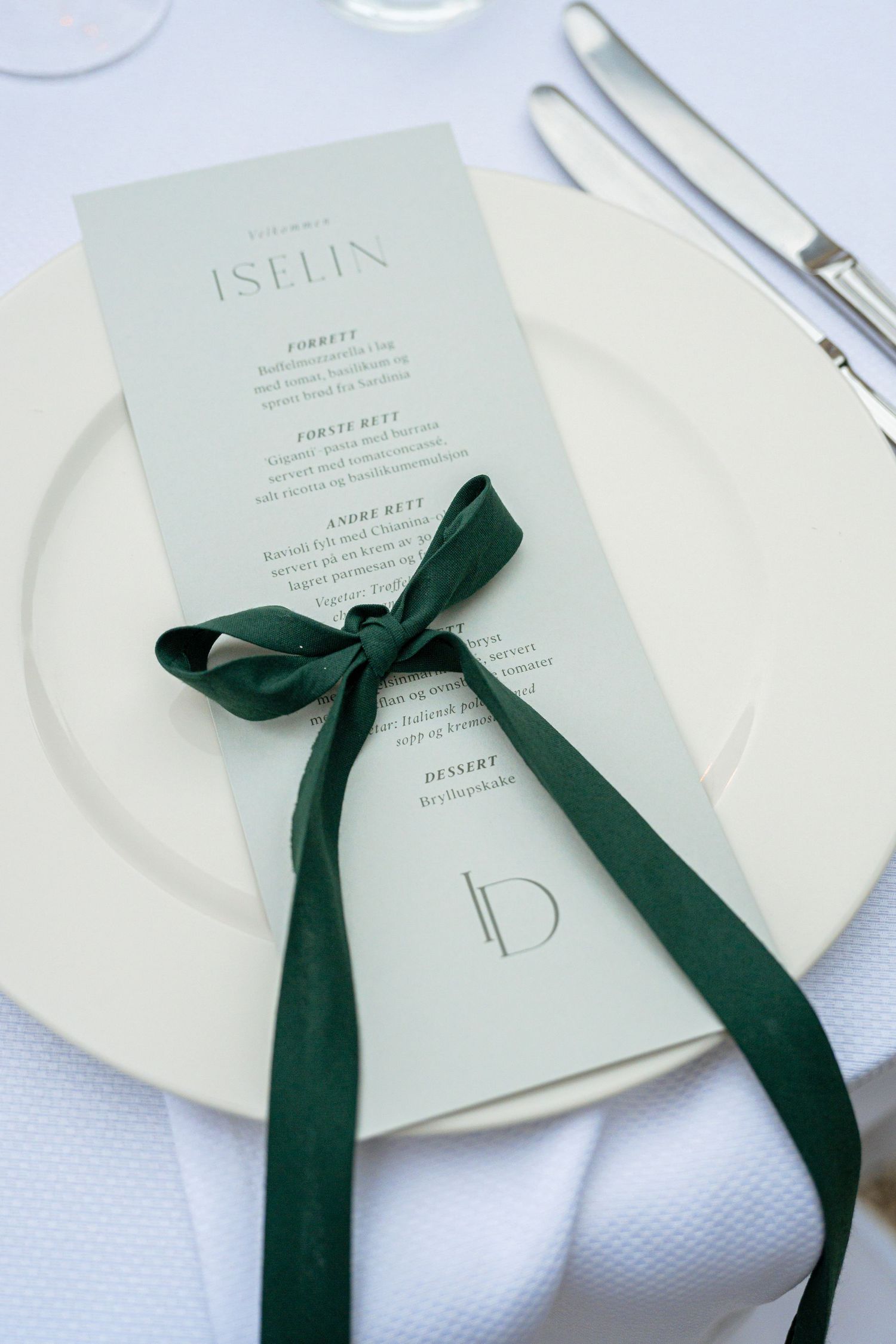 Elegant wedding menu card tied with dark green velvet ribbon on white plate with silverware.