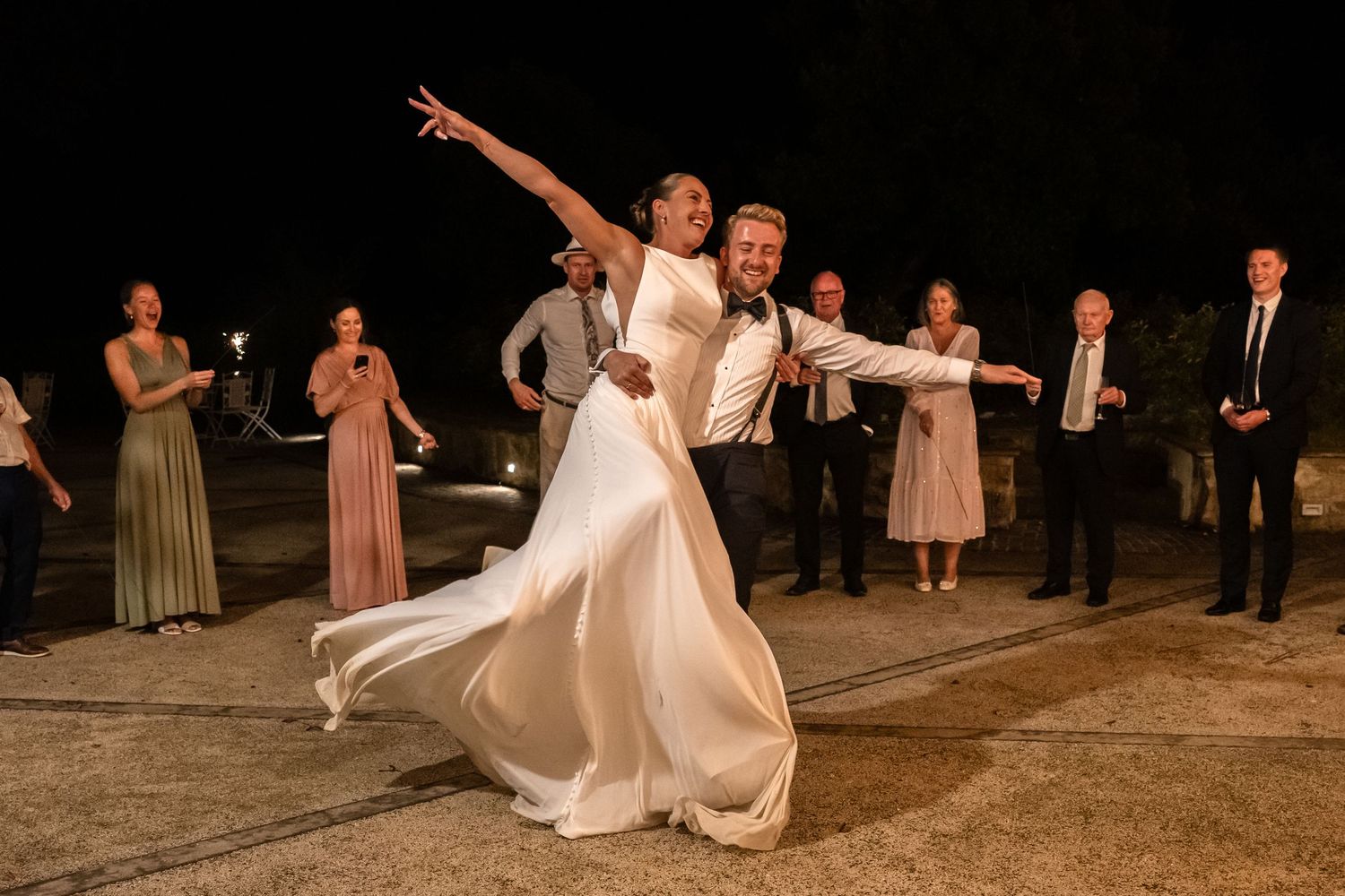 Bride and groom share a dramatic dance pose at their outdoor wedding reception at night with guests watching.