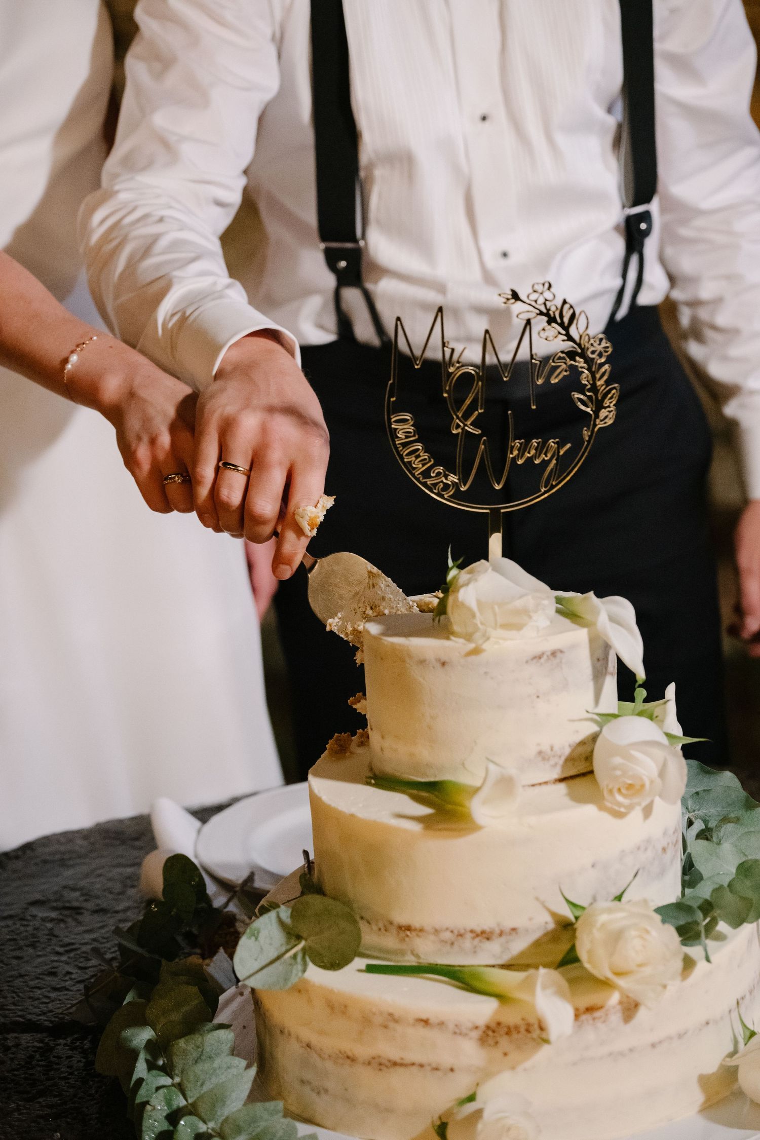 Bride and groom cutting a three-tier semi-naked wedding cake decorated with white roses and a Mr & Mrs cake topper.