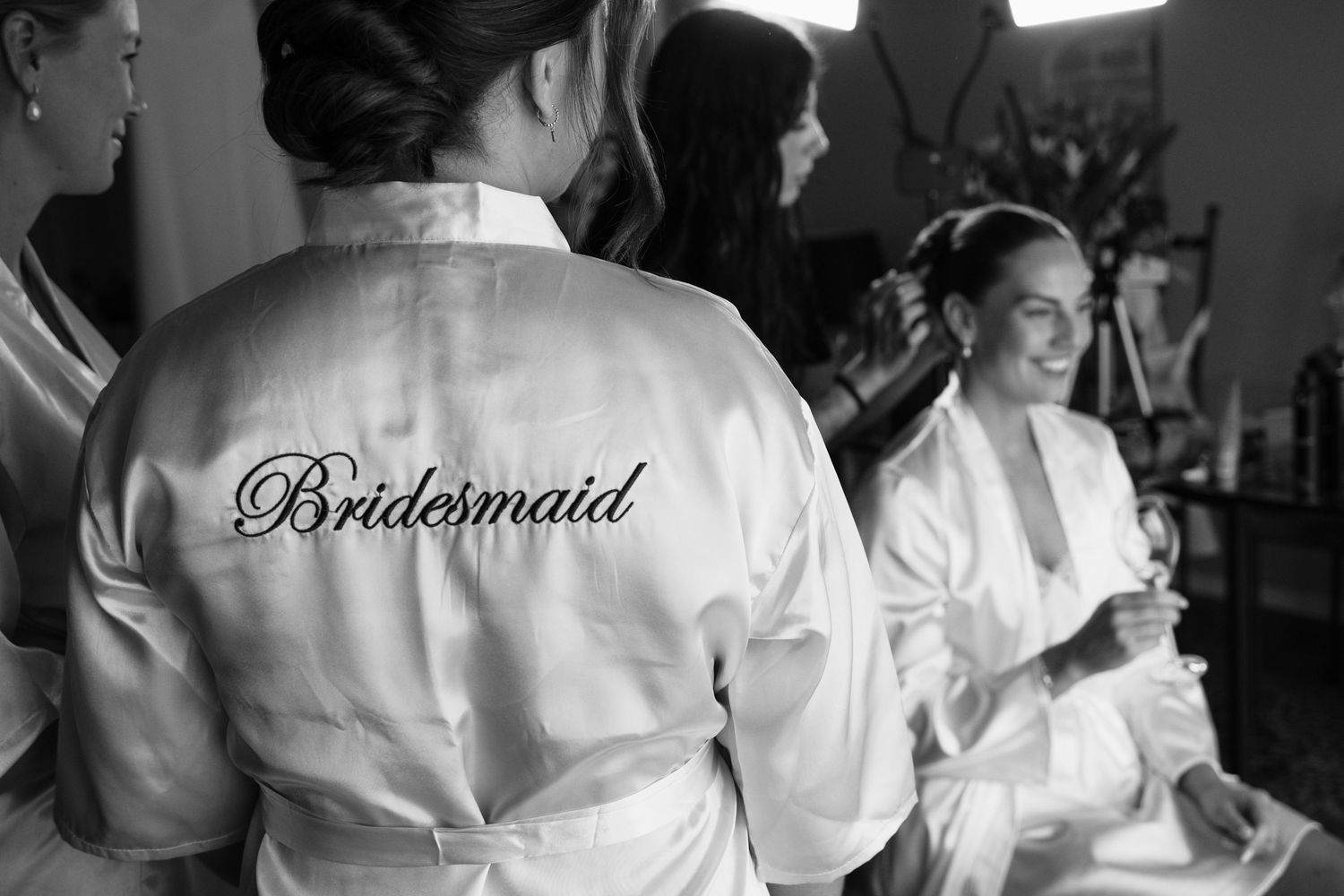 Black and white photo of bridesmaids in white robes with Bridesmaid script, preparing for a wedding ceremony.
