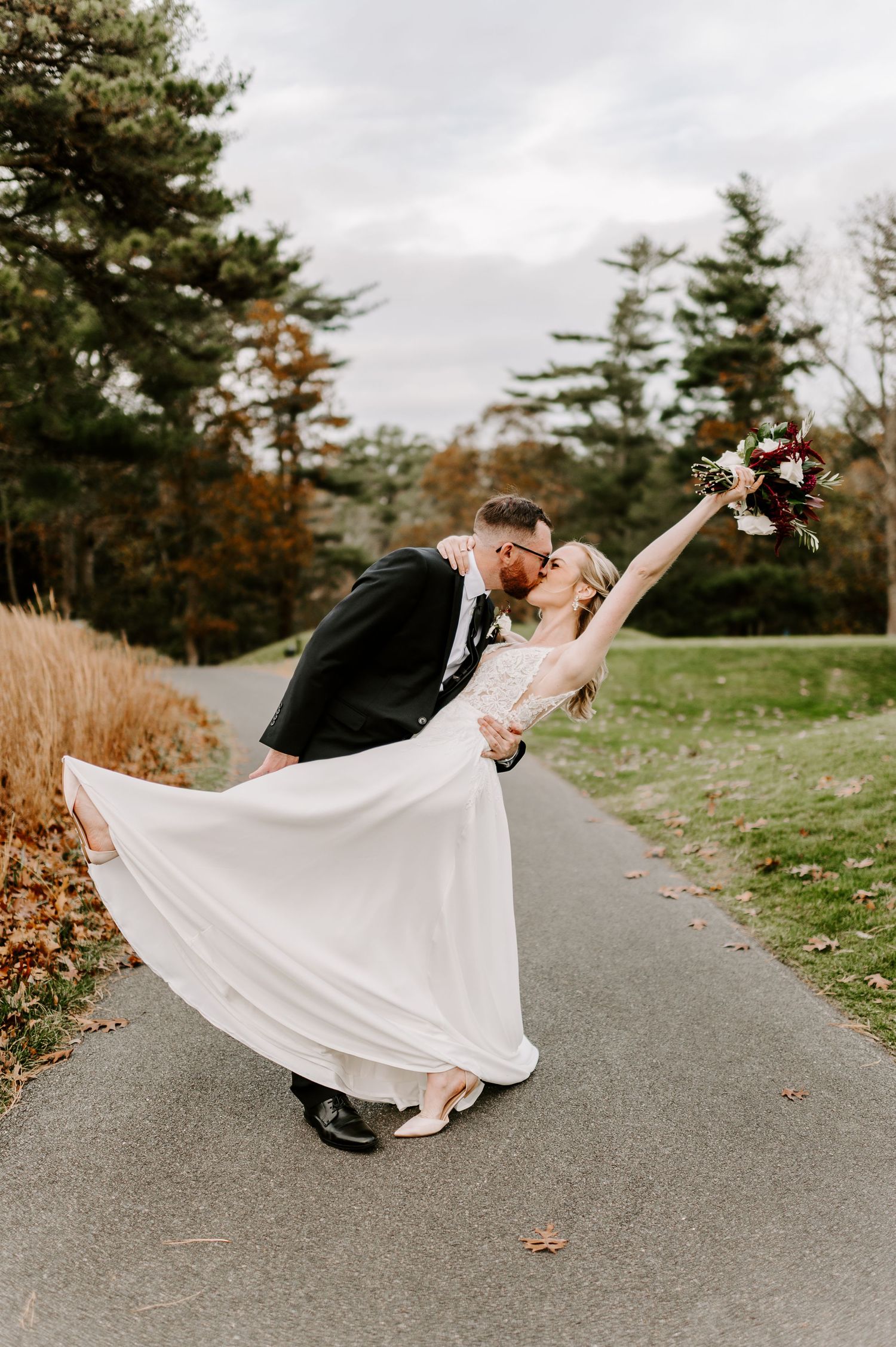 Dramatic dip pose during wedding photoshoot on a scenic autumn path.