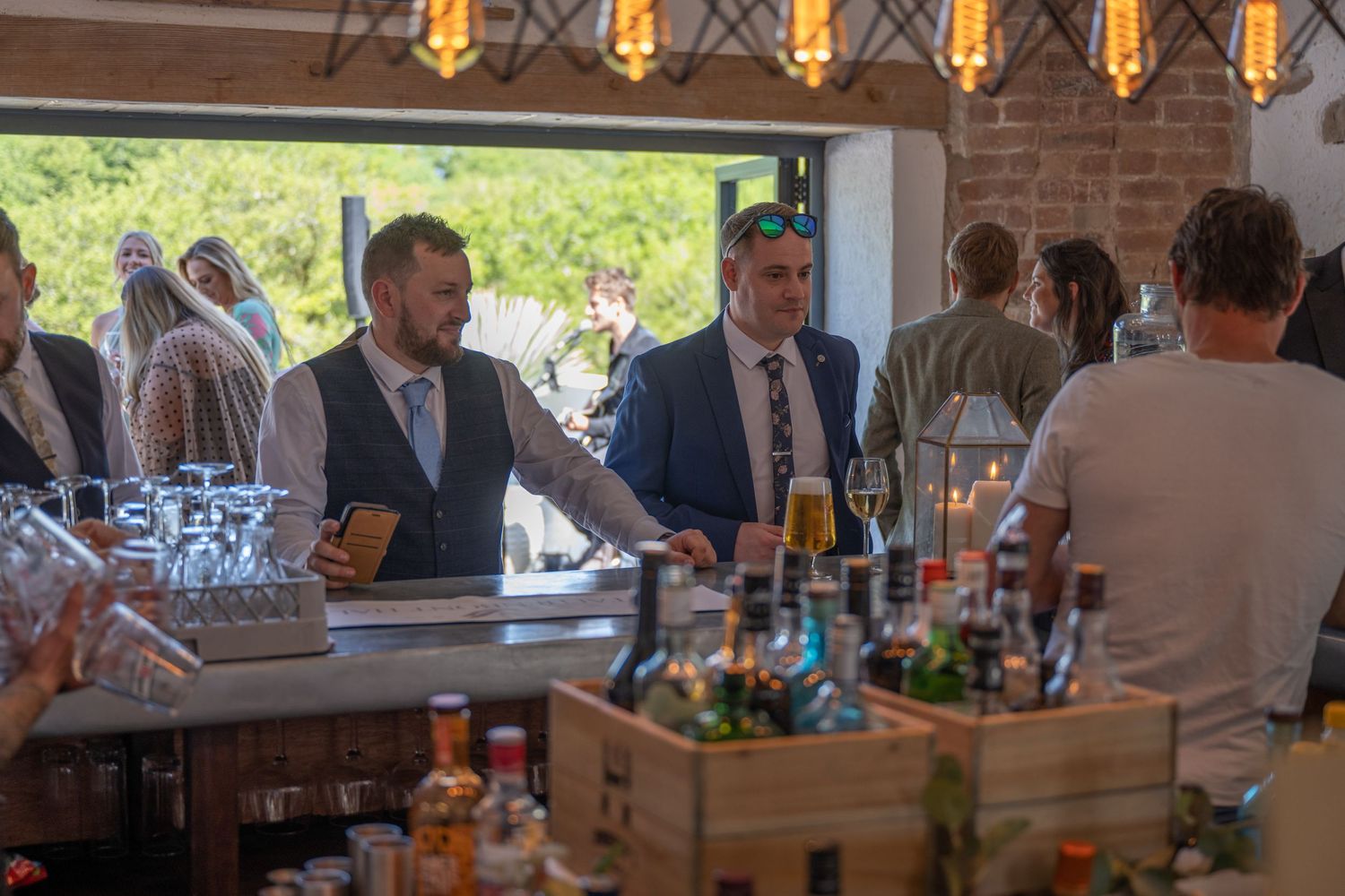 Wedding guests mingling at a bar area with bottles displayed in wooden crates.