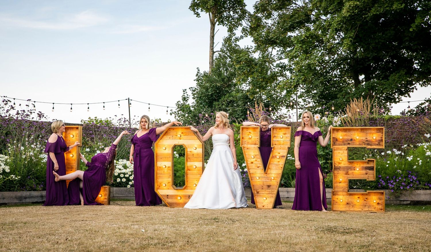 Decorative LOVE letters display with wedding party in purple dresses outdoors.