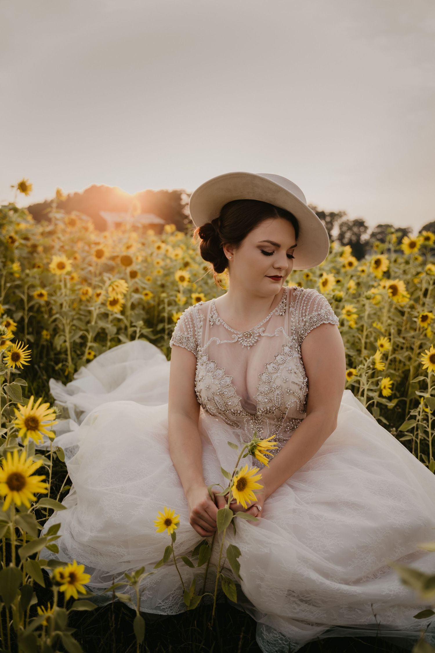 Woman in wedding dressing sitting in sunflower field at sunset