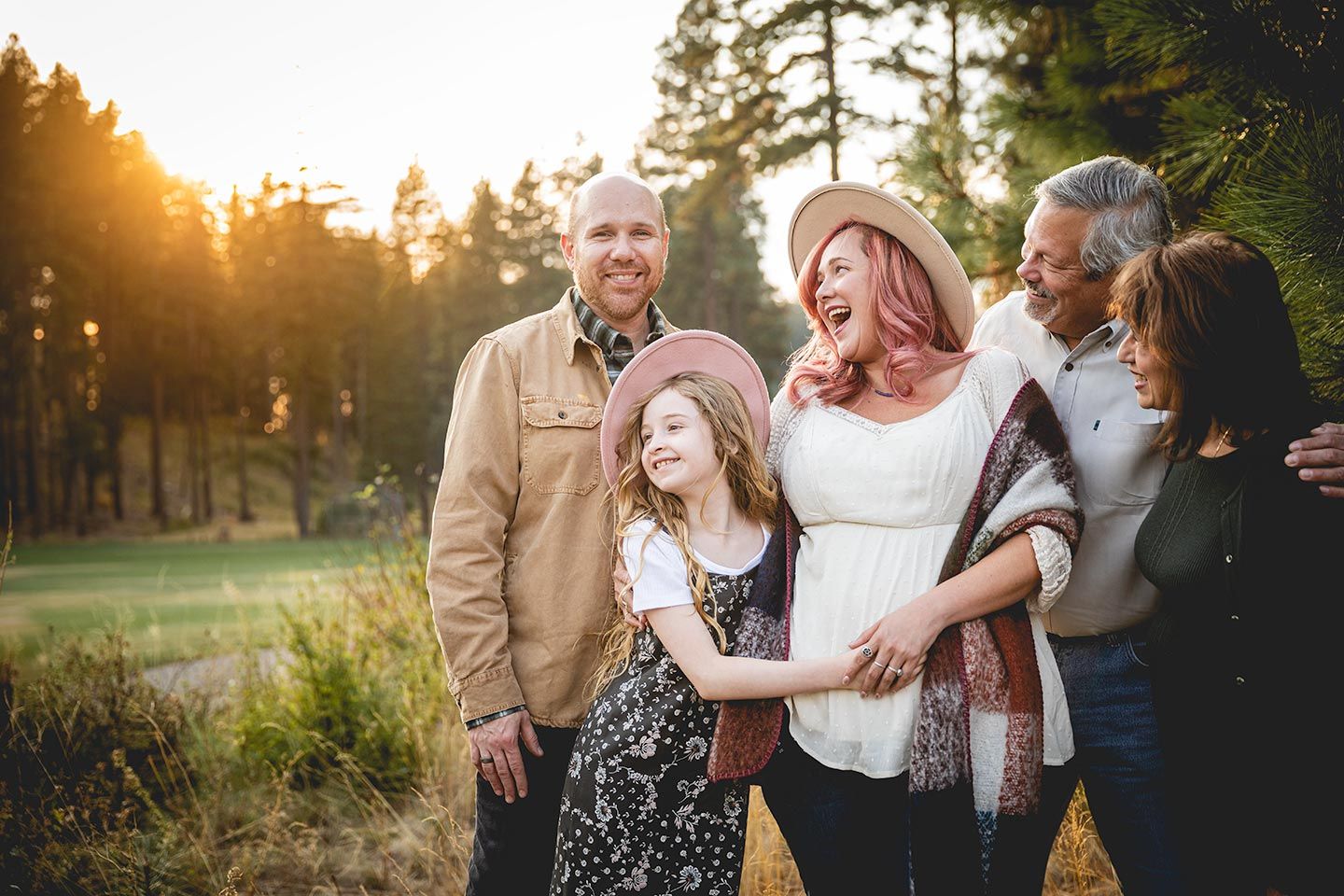 family hugging and standing near trees in a park while sun is setting