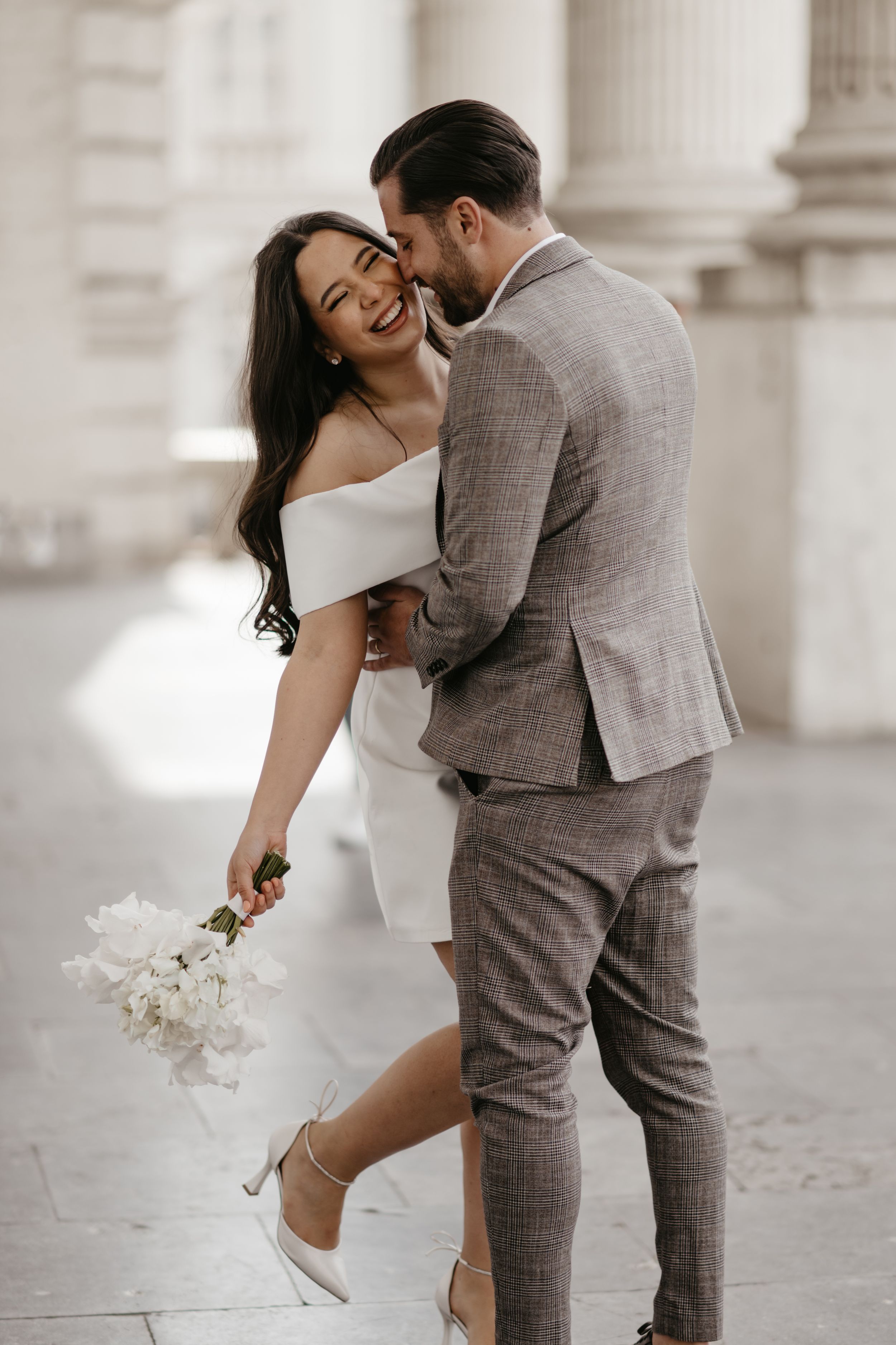 Joyful couple sharing a romantic moment in formal attire against classic architecture.