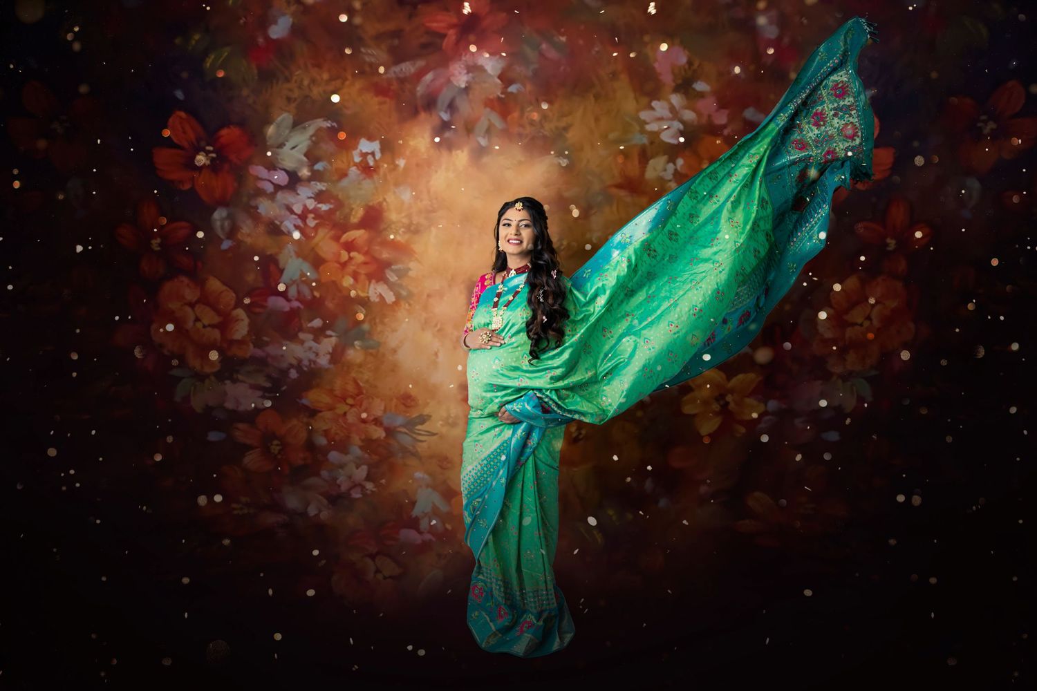 Ethereal maternity photo with flowing mint green dress against a cosmic galaxy backdrop with sparkles.