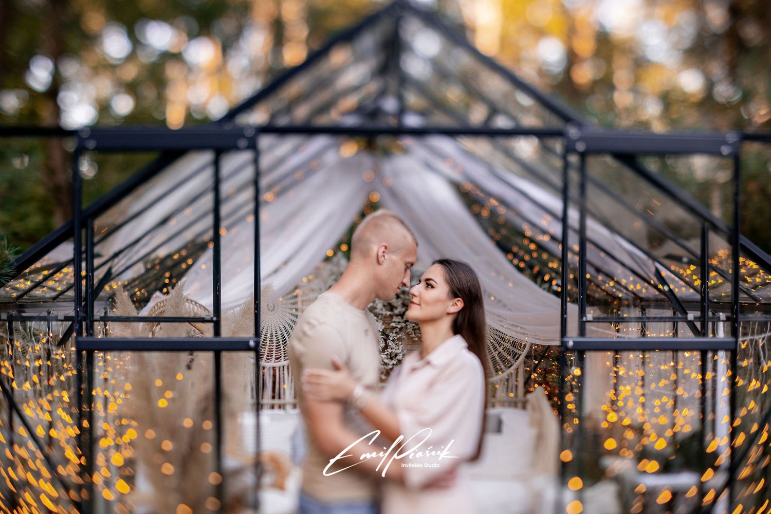 Romantic couple embraces in a greenhouse decorated with twinkling lights and bokeh effects.