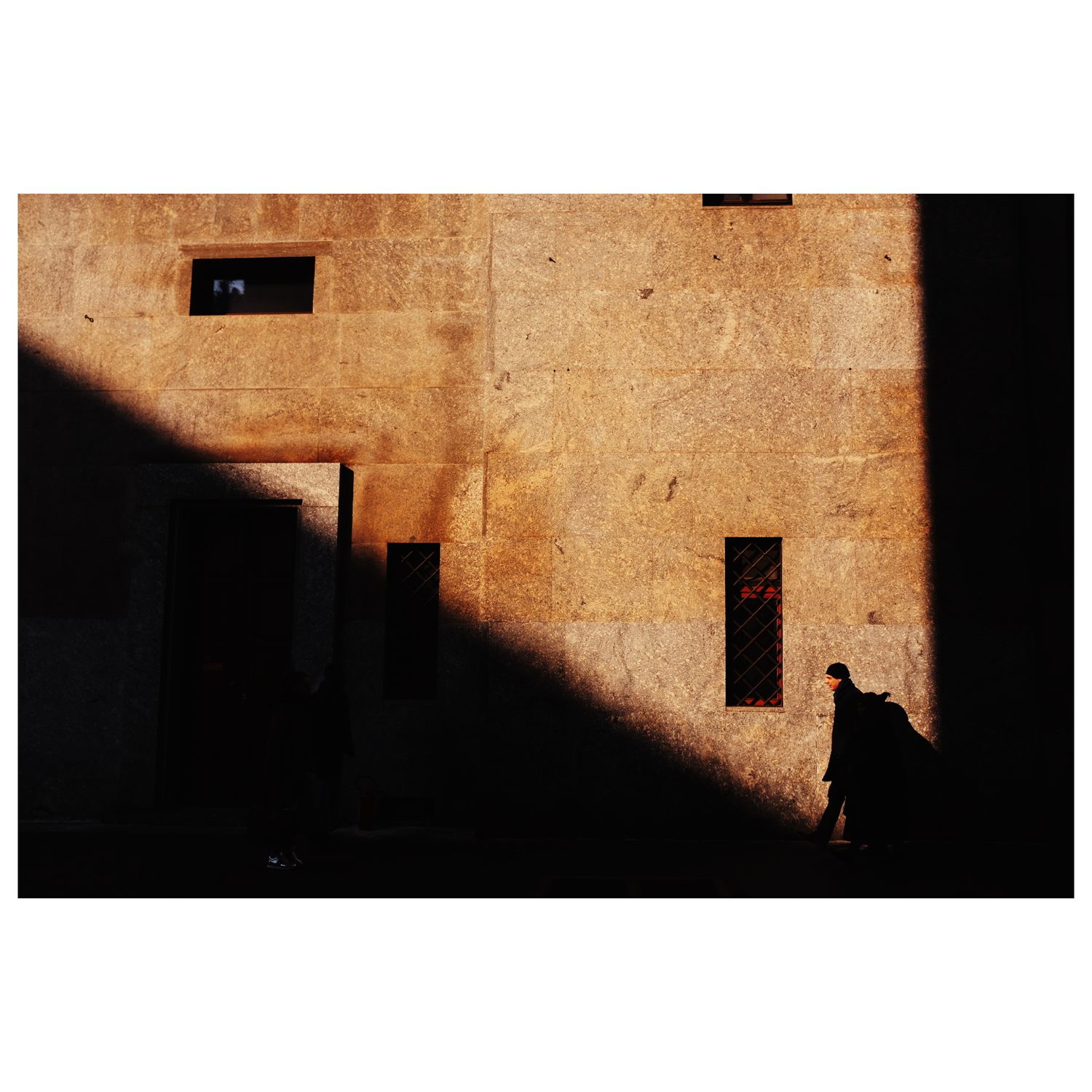 Textured stone wall with dramatic diagonal shadow line and architectural details.