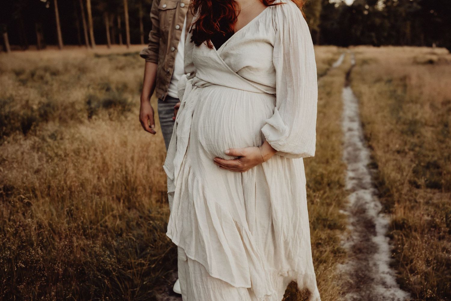 A maternity portrait showing a flowing white dress against a rustic outdoor background at sunset.