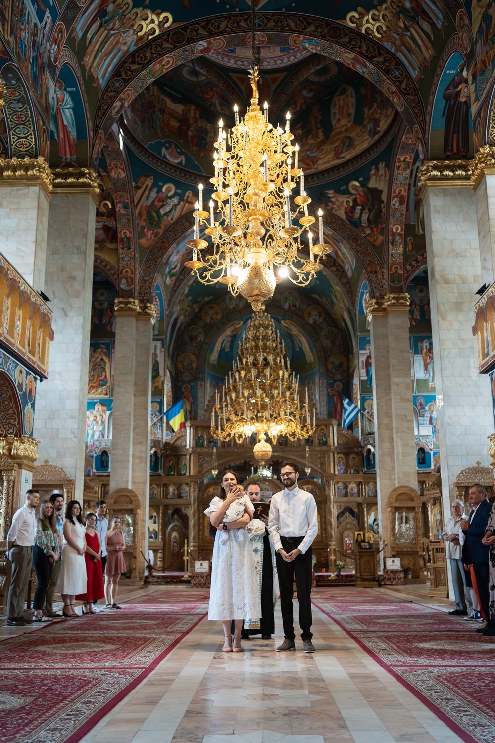 Ornate Orthodox church interior with crystal chandeliers and painted frescoes during a ceremony.