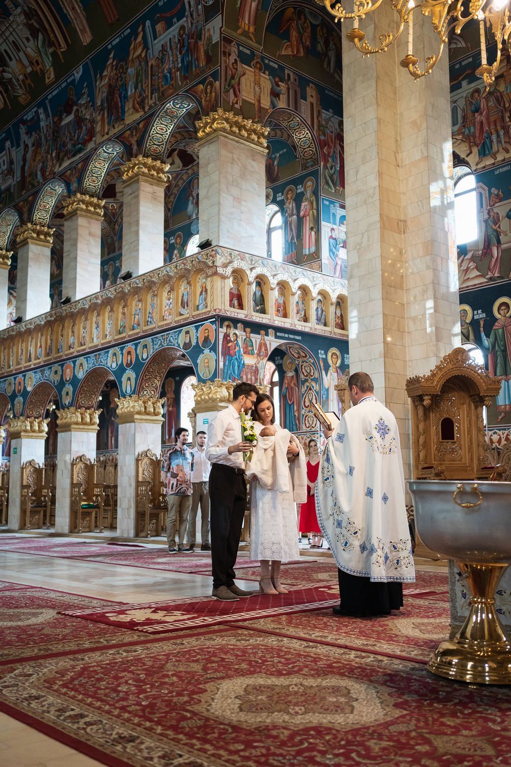 Orthodox church ceremony in progress showing detailed frescoes and red carpeted floor.