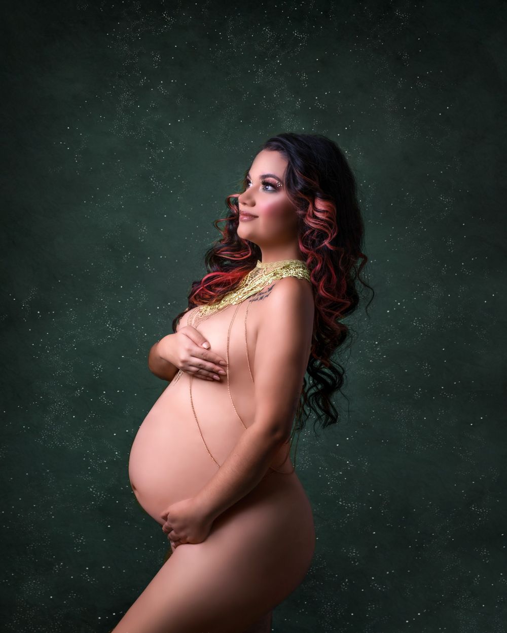 Artistic maternity photo with gold accents against textured green background.